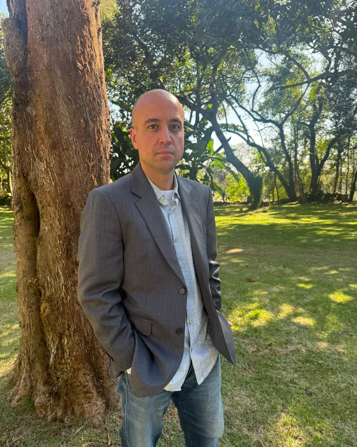Victor Marchiori, de paletó cinza, em pé ao lado de uma árvore